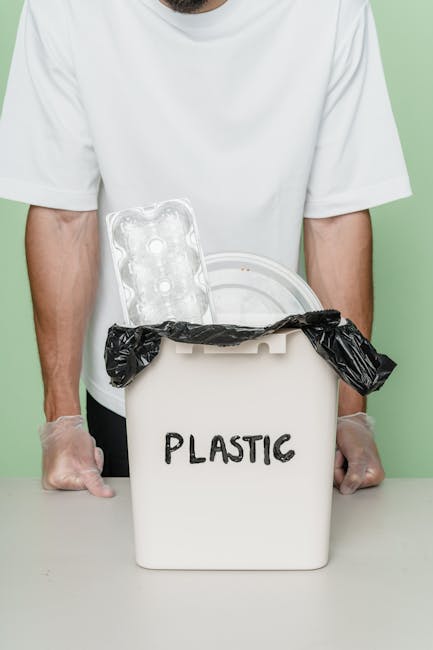 A person is seen disposing of paper waste into a white waste bin that has a partially visible label, with the lid open to reveal a brown paper bag inside. The individual is holding a crumpled paper bag in one hand while placing it into the bin, which is positioned on a wooden surface. In the foreground, another crumpled paper bag is held, appearing to contain additional waste. The environment appears to be an indoor setting, likely a kitchen or office space, with neutral lighting highlighting the textures of the paper bags and the smooth surface of the bin. The scene emphasizes the act of proper waste separation and disposal, aligning with private rubbish removal services offered by companies like rubbishremovalcrystalpalace.com, which assist with on-site clearance and alternative waste handling solutions to traditional council collections.